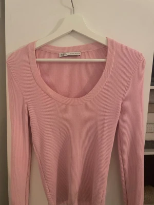 Rosa ribbad topp från Zara - Säljer en ljusrosa ribbad långärmad topp från Zara. Toppen har en rund halsringning och är tillverkad i ett stretchigt material som sitter snyggt på kroppen. Perfekt att styla med jeans eller kjol för en trendig look.