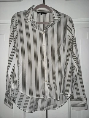 Vit och grön randig skjorta - Snygg vit skjorta med gröna vertikala ränder och klassisk krage. Skjortan har knappar framtill och långa ärmar med manschett. Materialet känns lätt och luftigt, perfekt för en stilren look.