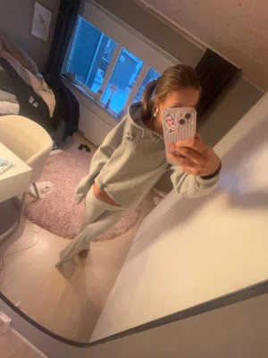 Grå hoodie med tryck och huva - Säljer en ljusgrå hoodie med svart tryck på ryggen där det står 'JE M'EN AMOUR' och en stjärna. Hoodien har en klassisk huva och en avslappnad passform, perfekt för en chill och trendig look. Storlek 158-164