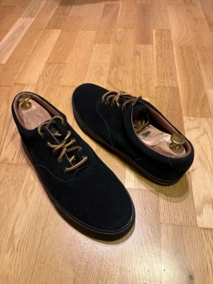 Ralph Lauren mocka sneakers - Lite schysstare svarta sneakers i mocka med bruna läder snören och svart sula🔥. Låg modell med rund tå och klassisk design⚡️. Perfekta för dig som gillar stilrena och tidlösa skor.👞 Skorna är knappt använda, enda tecknet på att de har använts är lite damm/smuts i sulan‼️