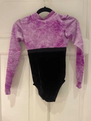 Gymnastikdräkt  - Säljer en av mina gamla AG gymnastikdräkter. Dräkten har lila/syrenfärgad överdel med glitter följt av svart nedre del. Lappen som sitter i dräkten har åkt av med storleken är 140-152. Nypris: 999 kr
