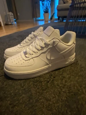 Nike Air Force 1 vita - Klassiska Nike Air Force 1 sneakers i helvitt skinn med rund tå och snörning. Ikonisk siluett med perforerad tåbox och platt sula. Perfekta för dig som gillar en clean och tidlös look.