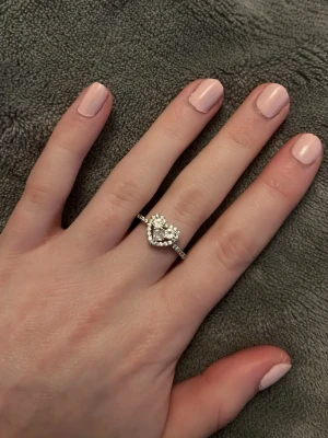 Silverring med hjärta och stenar - Säljer en snygg silverfärgad ring med ett hjärta i mitten, dekorerat med gnistrande små stenar runt om. Ringen har en tunn banddesign och hjärtat ger en romantisk touch. Perfekt för dig som gillar bling och vill ha något extra på fingret.Vid köp av fler ringar kan jag slå ihop annonserna så frakten blir billigare.