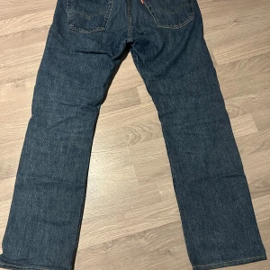 Levi's 501 mörkblå jeans straight fit - Klassiska Levi's 501 jeans i mörkblå tvätt med raka ben och femficksmodell. Jeansen har normal passform och är tillverkade i slitstarkt denimtyg av bomull. Perfekta för dig som gillar tidlös stil och vill ha ett par riktigt schyssta jeans.