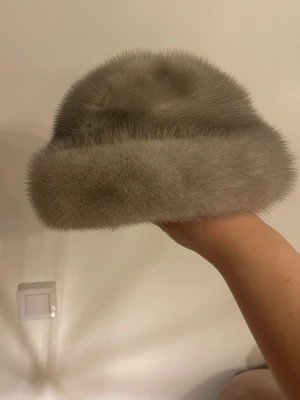 Ljusgrå pälsmössa med sidenfoder - Supersnygg ljusgrå pälsmössa med mjukt, fluffigt yttre och glansigt sidenfoder på insidan. Klassisk rund form som ger en lyxig vintagekänsla och passar perfekt till kalla dagar. Mössan är stilren och elegant, perfekt för dig som vill sticka ut.