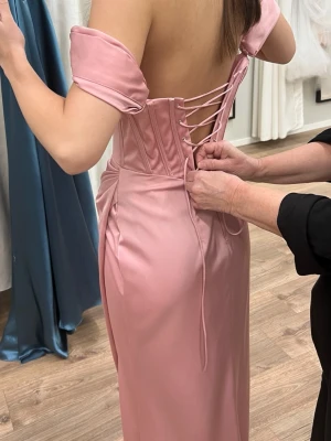 balklänning rosa - Supersnygg rosa balklänning i satinliknande material med offshoulder-ärmar och snörning i ryggen. Klänningen har en elegant slits framtill och markerad midja. Perfekt för bal! helt ny och oanvänd med lapp kvar! 🥰