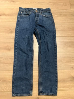 Jack&Jones  mörkblå raka jeans - Klassiska Jack&Jones jeans i mörkblå tvätt med rak passform. Jeansen har fem fickor, knappgylf och är tillverkade i slitstarkt bomullsjeans. Perfekta för dig som gillar tidlös och enkel stil.