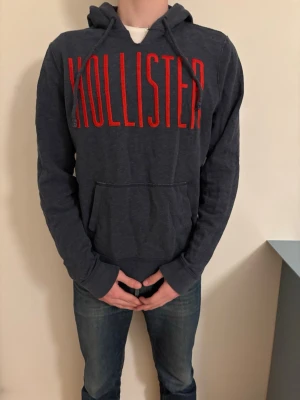 Mörkblå  Vintage hoodie från Hollister - Snygg mörkblå eftertraktad hoodie från Hollister med stor röd logga över bröstet. Klassisk känguruficka framtill och justerbar huva med dragsko. Perfekt för en avslappnad och trendig stil. Tillverkad i mjukt material för extra komfort.
