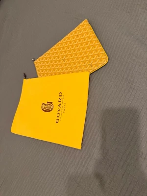 Gul  kuvertväska med mönster - Säljer en gul kuvertväska med  ikoniska grafiska mönster. Väskan har en smidig dragkedja upptill och kommer med original dustbag. Perfekt för dig som vill ha något unikt och trendigt i din väsksamling. Helt ny! Mvh ItsForfits 🌟🌟🌟