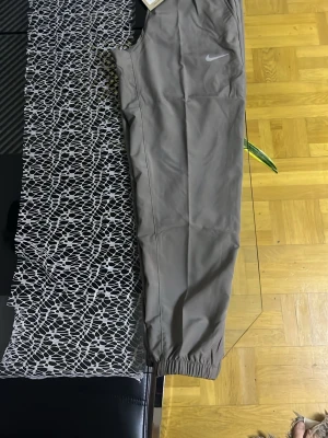 Bruna mjukisbyxor från Nike - Snygga bruna mjukisbyxor från Nike med klassisk logga på benet. Byxorna har resår i bensluten och en avslappnad passform. Perfekta för chill eller träning, och tillverkade i mjukt material för extra komfort.