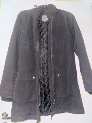 Svart jacka  - Svart parkas från Race Marine med quiltat innerfoder och dragkedja framtill. Jackan har stora fickor med tryckknappar, hög krage och justerbar huva. Behövs en tvätt annars i fint skick. 