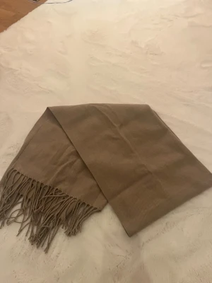 Beige stickad halsduk - Mysig beige halsduk i stickat med fina fransar längst ut. Perfekt för kalla dagar och gör outfiten lite bättre. Aldrig använd 
