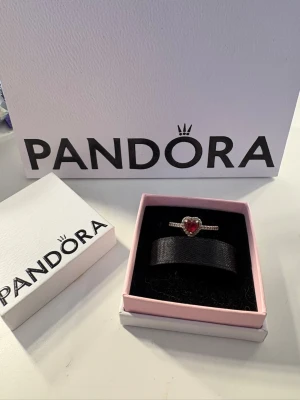 Pandora silverring med röd hjärtformad sten - Snygg ring från Pandora i silver med en röd hjärtformad sten i mitten. Säljer då den ej kommer till användning. Storlek 52 som motsvarar 16.50 i mm