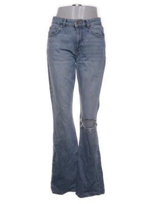 Blå bootcut jeans med slitning - Snygga blå bootcut jeans med hög midja och slitning över ena knät. Jeansen har klassisk femficksdesign och är tillverkade i mjukt denimtyg. Perfekta för en avslappnad och trendig look.