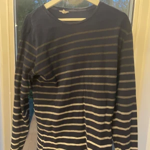 Mörkblå randig tröja från Armor Lux - Säljer en mörkblå långärmad tröja från Armor Lux med smala horisontella vita ränder. Tröjan har en klassisk rund hals och är gjord i mjuk bomull, perfekt för dig som gillar enkel och stilren design.