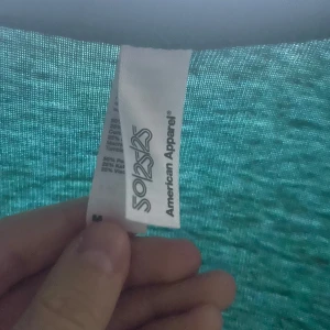 Turkos kofta från American Apparel - Säljer en tunn turkos kofta från American Apparel i storlek M. Koftan har långa ärmar, två fickor framtill och knäppning med knappar. Materialet är en mix av polyester, bomull och viskos vilket gör den mjuk och lätt. Perfekt att slänga på sig över en t-shirt.