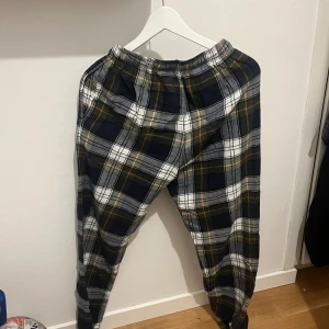 Rutig byxa med resår och snörning - Snygga rutiga byxor från Cubus i mörkblått, vitt och lite orange. Byxorna har resår i midjan och snörning för extra komfort. Tillverkade i mjukt bomullstyg, perfekta för en chill och avslappnad stil. Skick 8/10 och är använda i få tillfällen 