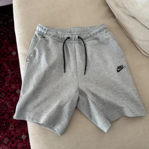 Grå Nike shorts med snörning - Säljer ett par gråa shorts från Nike med svart snörning i midjan och logga på vänster ben. De har en avslappnad passform och är tillverkade i mjukt bomullsmaterial, perfekta för chill eller träning. Fickor på sidorna för extra funktion.