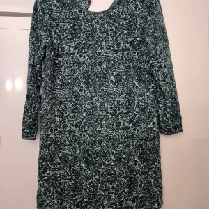 Klänning - Snygg klänning från Jacqueline de Yong i storlek 38. Klänningen har ett blått, turkos och vitt paisleyinspirerat mönster, v-ringad hals och långa ärmar. Materialet är mjukt och lätt, perfekt för dig som gillar bekväma och trendiga plagg.