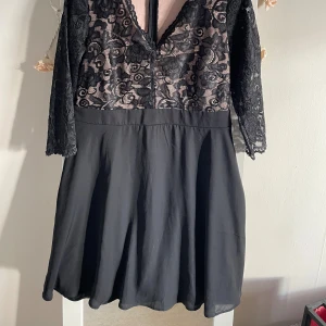 Svart spetsklänning från Bodyflirt - Supersnygg svart kortklänning från Bodyflirt med spets upptill och halvtransparenta trekvartsärmar. Kjolen är slät och faller fint. Toppen har blommigt spetsmönster och v-ringning framtill. Perfekt för dig som vill sticka ut lite extra!