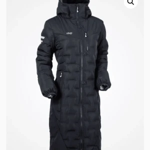 Mörkblå långkappa från Uhip - Lång svart dunjacka från Uhip med hög krage, huva och flera dragkedjor. Jackan har quiltad design, långa ärmar med resår vid handlederna och praktiska fickor. Perfekt för kalla dagar när du vill hålla dig varm och bekväm. Skriv för fler bilder🩷