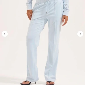 Ljusblå Juicy Couture mjukisbyxor - Supermjuka ljusblå mjukisbyxor från Juicy Couture med breda ben, snörning i midjan och glittriga stenar som bildar 'Juicy' på baksidan. Byxorna har fickor med dragkedja och en liten logga framtill. Säljer då dom inte kommer till användning!