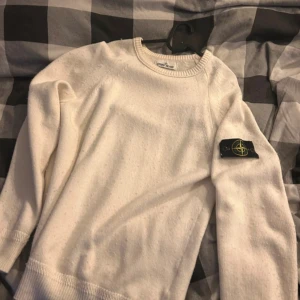 Vit stickad tröja från Stone Island - Säljer en clean vit stickad tröja från Stone Island med klassisk patch på ärmen. Tröjan har rund halsringning, ribbade muddar och är långärmad. Perfekt för dig som gillar stilren och enkel design med premiumkänsla.