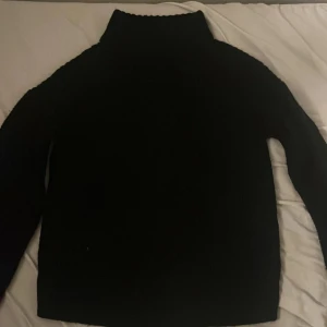 Svart polotröja från VILA - En svart polotröja från VILA i storlek S. Tröjan är stickad med hög krage och har långa ärmar. Perfekt för kyligare dagar och enkel att matcha med olika outfits.