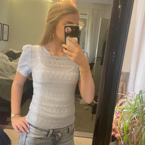 Ljusblå spetsblus med puffärm - Supersöt ljusblå blus i spets med korta puffärmar och rund halsringning. Blusen har ett detaljerat spetsmönster över hela och sitter figurnära. Perfekt att styla med jeans för en fräsch look.