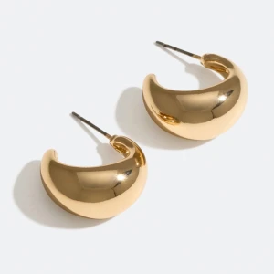 Chunky guldörhängen i bågform - Säljer ett par chunky örhängen i bågform med blank, guldig finish. De har en modern och stilren design som verkligen syns. Perfekta för dig som gillar statement-smycken och vill addera lite extra glans till din look.