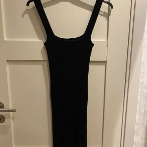 Svart ribbad långklänning Stradivarius - Svart långklänning från Stradivarius i ribbad stickad kvalitet. Klänningen är ärmlös med breda axelband och har en tight passform som framhäver figuren. Perfekt för dig som gillar minimalistisk och stilren look.