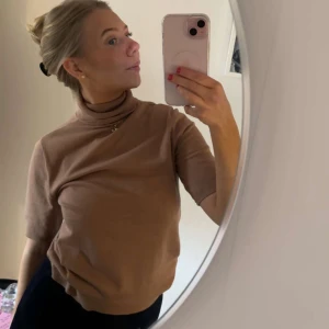 Beige polotröja från Anne Klein - Snygg beige polotröja från Anne Klein med korta ärmar och ribbad krage. Blivit lite spräcklig i tvätten men annars inga fel