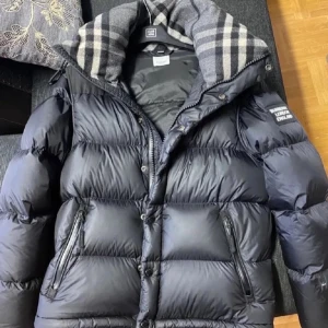 Svart pufferjacka från Burberry London - Säljer en svart pufferjacka från Burberry London med klassisk rutig insida på kragen. Jackan har dragkedja och knappar framtill, två fickor med dragkedja och en patch på ärmen. Perfekt för kalla dagar och riktigt snygg streetstil.