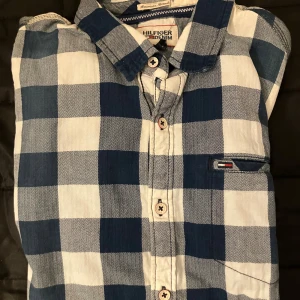 Blårutig skjorta från Hilfiger Denim - Blårutig skjorta från Hilfiger Denim i storlek M. Skjortan har klassisk krage, långa ärmar med manschett och knappar framtill. Materialet är mjuk bomull och mönstret är stora blå och vita rutor. Liten logotypdetalj vid bröstfickan för extra stilpoäng.