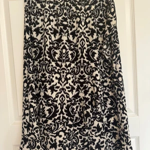 Svartvit långkjol från ONLY - Säljer en svartvit långkjol från ONLY med ett coolt abstrakt mönster. Kjolen är tillverkad i mjuk polyester med lite stretch för extra komfort. Passformen är normal och tyget har en snygg struktur som ger kjolen en unik look.