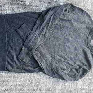 Mörkgrå merinoullströja H&M - Säljer en stilren mörkgrå långärmad tröja från H&M i mjuk merinoull. Tröjan har rund halsringning och ribbade muddar vid ärmslut och nederkant. Perfekt för lager-på-lager under kyliga dagar.