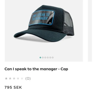 Svart keps med textplatta - Svart keps från Dockhatter & Co med böjd skärm och mesh på baksidan. Framtill sitter en blank platta med blå kant och texten 'CAN I SPEAK TO THE MANAGER' i blått. Perfekt statement-piece för dig som vill sticka ut.