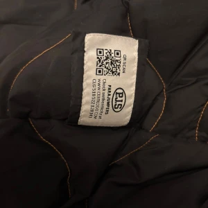 Svart Parajumpers pufferjacka XXL - Svart pufferjacka från Parajumpers Masterpiece Series med snygga broderade patchar och orange detaljer. Jackan har slim fit och är tillverkad i slitstark polyester, perfekt för kalla vinterdagar. Klassisk look med coola detaljer och grym passform.