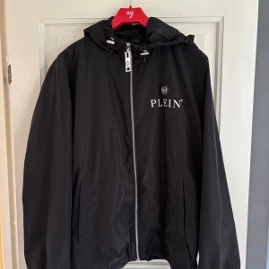   Philipp Plein wind breaketlimited edition äkta - Svart vindjacka från Philipp Plein med huva, silverfärgad dragkedja med dödskalle-detalj och logga på bröstet. Jackan har justerbara snören vid huvan och två fickor framtill. Snygg och stilren design med coola detaljer.VILL SÄLJA DE EFTERSOM DEN INTE PASSAR SKRIV PRIVAT OM DU VILL HA BEVIS PÅ KVITTO