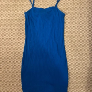 Blå ribbad klänning från Amisu - Säljer en blå ribbad klänning från Amisu i storlek 36. Klänningen är kort, har smala axelband och är figurnära. Perfekt för dig som gillar enkel och stilren design med en poppig färg.