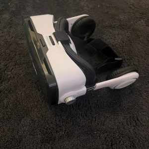 VR200 Virtual Reality Box - Prixton VR200 Virtual Reality Box med inbyggda hörlurar. Justerbara remmar och ratt för optimal passform. Passar de flesta smartphones. Produkten är  i gott skick utan synligt slitage eller defekter. Perfekt för VR-upplevelser hemma.