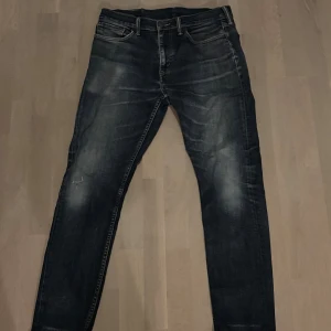 Levi's 515 mörkblå jeans - Snygga Levi's 515 jeans i mörkblå tvätt med slitningar och klassiska fem fickor. Jeansen har en smal passform och raka ben, med detaljer som synliga sömmar och läderpatch bak i midjan. Perfekta för en avslappnad och trendig look.