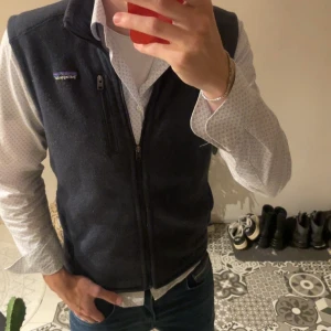 Svart fleeceväst från Patagonia - Svart fleeceväst från Patagonia med hög krage och dragkedja framtill. Västen har en bröstficka med dragkedja och två sidofickor. Perfekt för lager-på-lager och har en stilren, enkel design med diskret logga på bröstet. Storlek M. Är 186cm och den passar perfekt! Västen är knappt använd och inga defekter eller sådant!