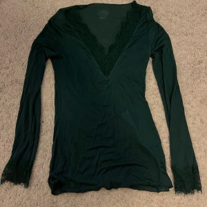 Mörkgrön topp med spets från Intimissimi - Supersnygg mörkgrön långärmad topp från Intimissimi med djup v-ringning och spetsdetaljer vid halsringning och ärmslut. ❤️