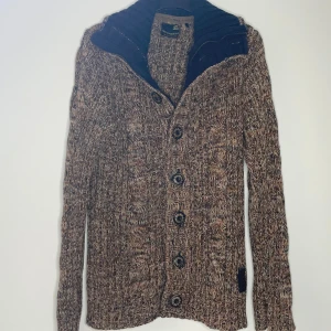 Brunmelerad stickad kofta No Excess - Säljer en brunmelerad stickad kofta från No Excess med grovstickat mönster, stora knappar och ribbad krage i mörkblått. Koftan har lång ärm och både knappar och dragkedja framtill. Perfekt för lager-på-lager under kyliga dagar.