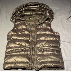 BVALDI Väst - En varm väst med två fickor på utsidorna  om västen och 1 ficka på insidan. Man kan även ta av och sätta på luvan passar dig som har M