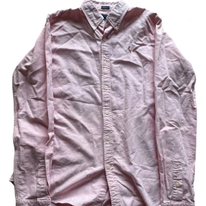 Rosa skjorta från Ralph Lauren - Snygg rosa skjorta från Ralph Lauren i slim fit-modell. Skjortan är tillverkad i 100% bomull och har klassisk button down-krage, långa ärmar och broderad logga på bröstet. Perfekt för dig som gillar stilrena och tidlösa plagg.