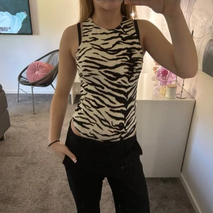 Zebramönstrad ärmlös body  - Säljer en snygg ärmlös body med zebramönster i svart och vit. Toppen har rund halsringning och sitter tight mot kroppen. Perfekt för dig som vill sticka ut med ett djurmönster och gillar trendiga detaljer.