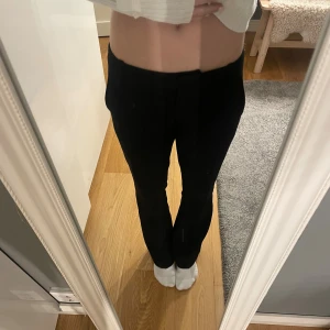 Svarta kostymbyxor med bootcut - Säljer ett par svarta utsvängda kostymbyxor med låg midja. Byxorna har en klassisk look med raka ben som blir lite utsvängda nertill. Perfekta att styla med sneakers eller boots för en clean vibe.