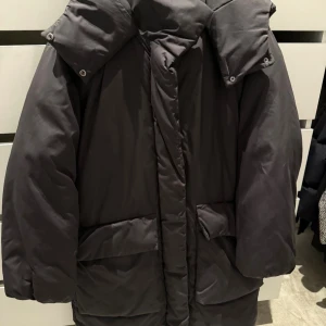 Svart lång pufferjacka med huva - Säljer en svart pufferjacka med stor huva och rejäla fickor. Jackan är lång och har en klassisk, oversized passform som håller dig varm under kalla dagar. Perfekt för dig som vill ha en stilren och enkel vinterjacka. Säljer den för 200kr